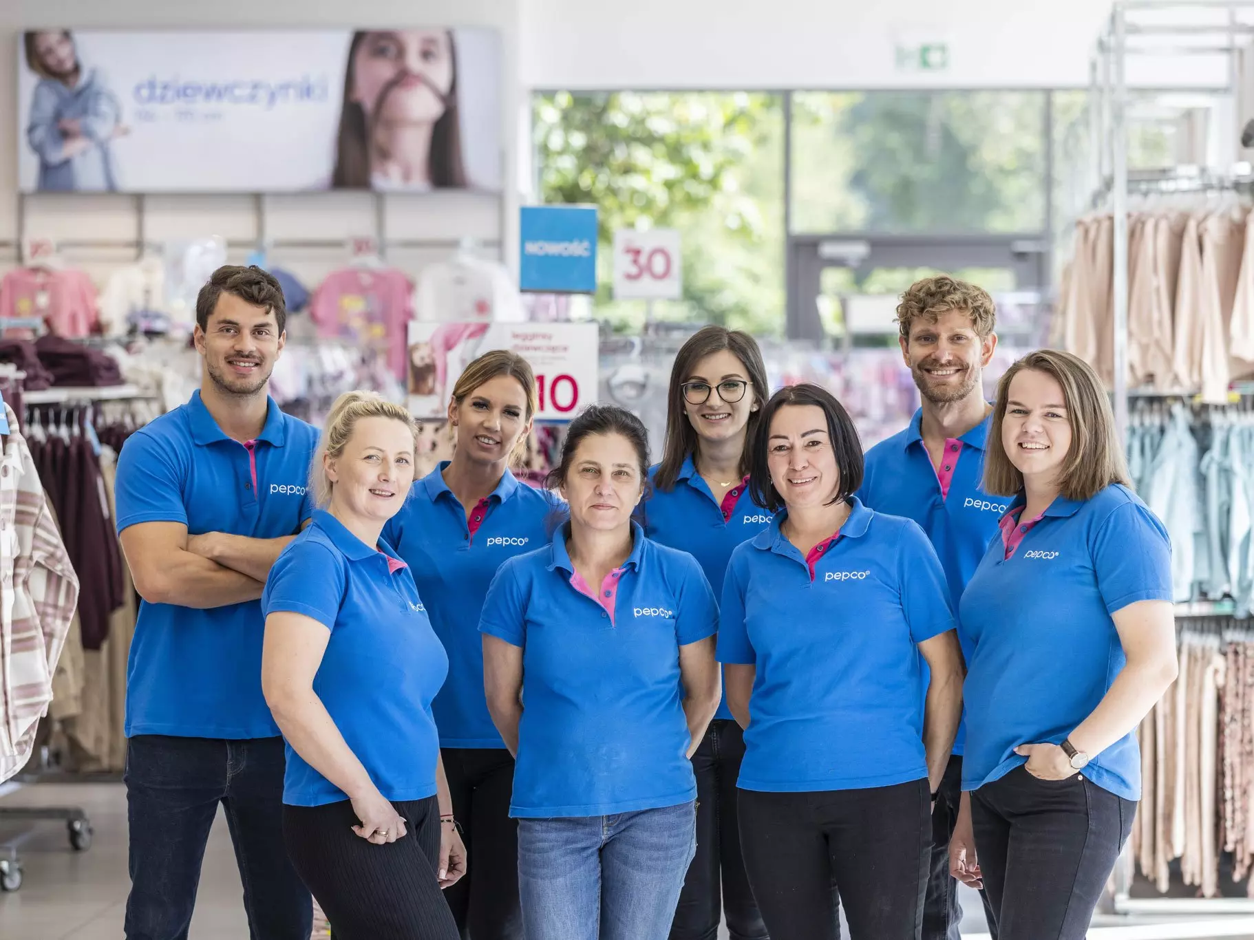 Equipo de Pepco con camisetas polo azules posando en el interior de una tienda con ropa y carteles promocionales.